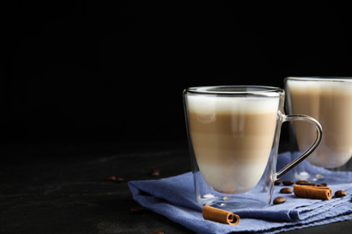 Photo of Delicious latte macchiato, cinnamon and coffee beans on grey table against black background. Space for text