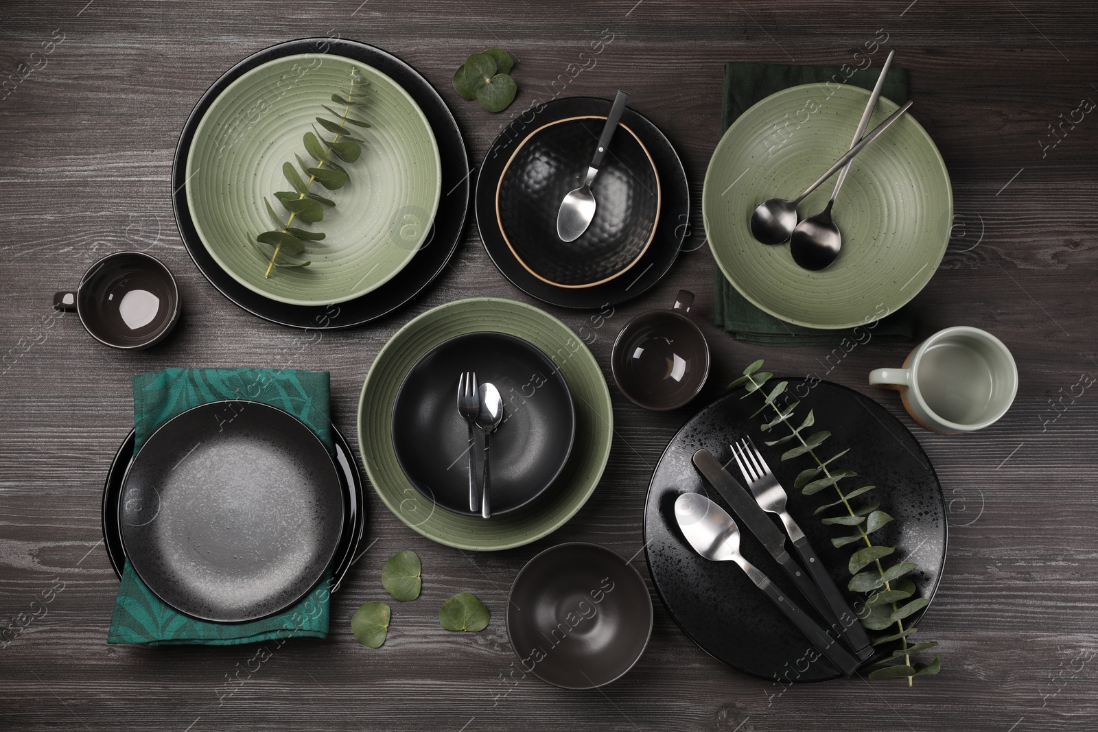 Photo of Stylish table setting with cutlery and eucalyptus branches on dark wooden background, flat lay