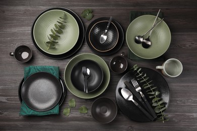 Stylish table setting with cutlery and eucalyptus branches on dark wooden background, flat lay