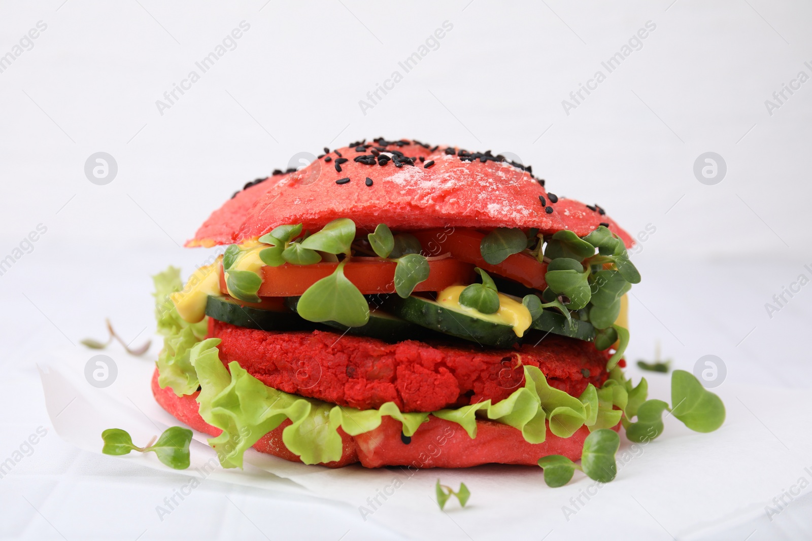 Photo of Tasty pink vegan burger with vegetables, patty and microgreens on white tiled table, closeup