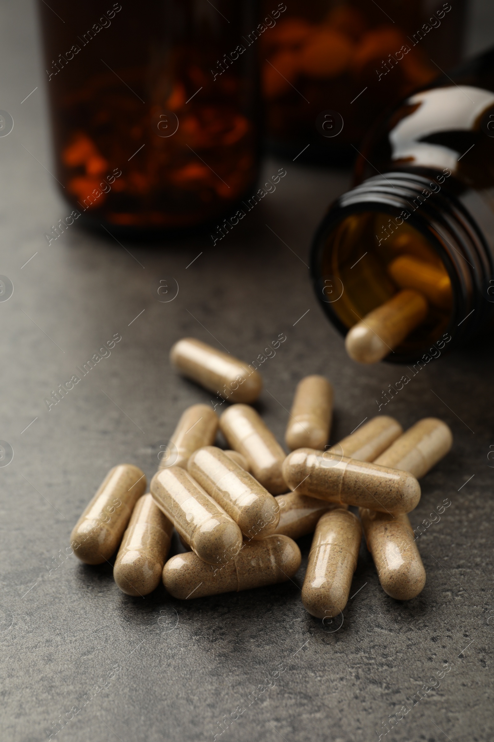 Photo of Overturned bottle with dietary supplement capsules on grey table, closeup