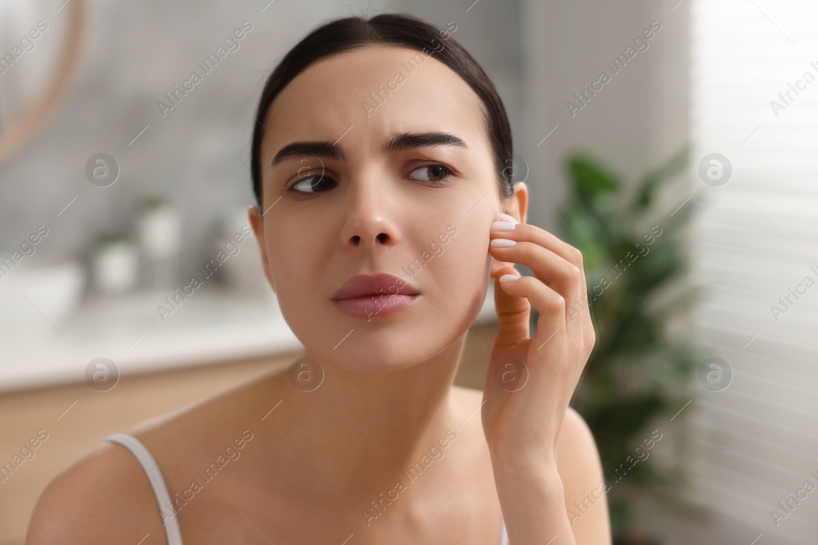 Photo of Woman with dry skin looking at mirror indoors