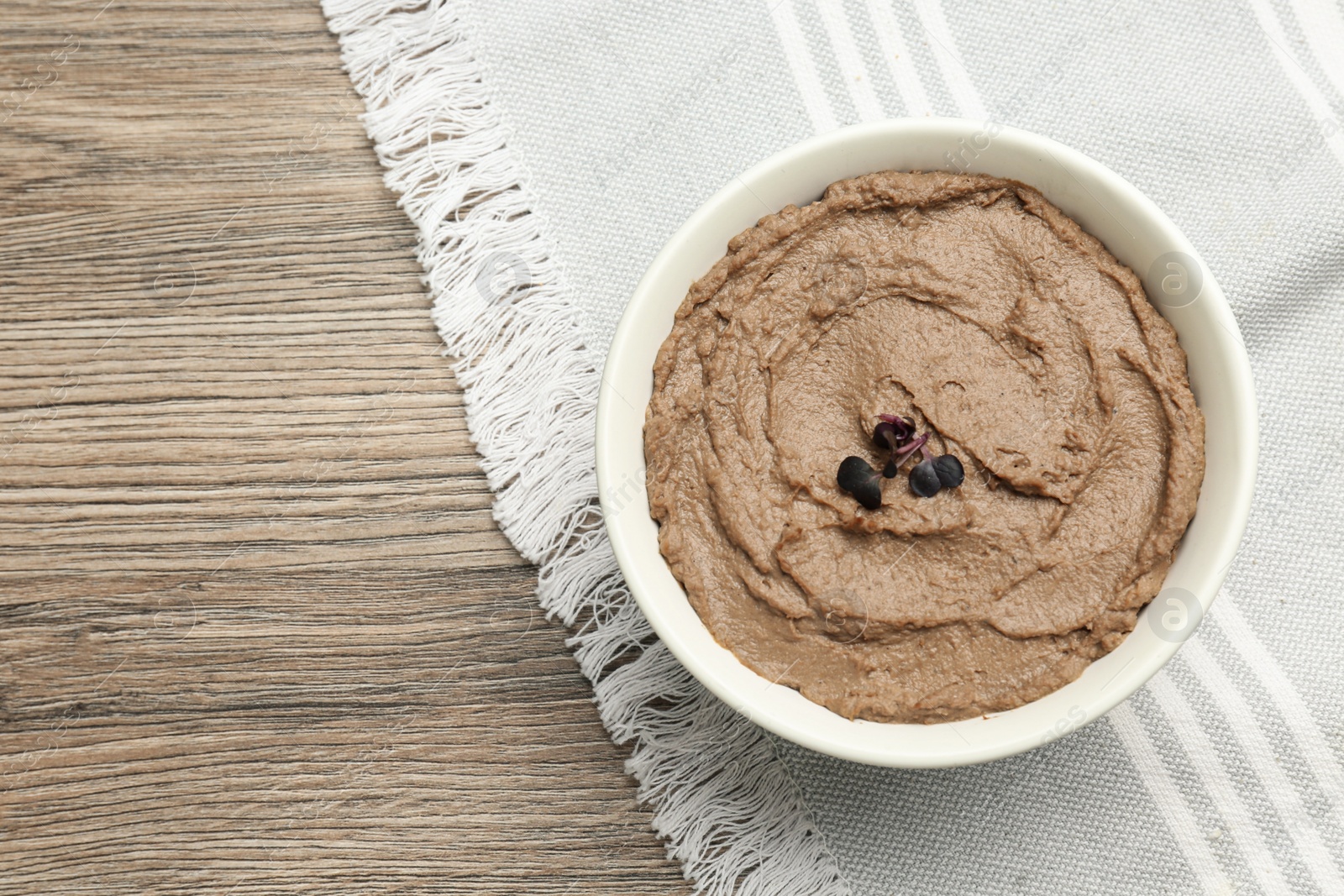 Photo of Tasty liver pate with herb in bowl on wooden table, top view. Space for text