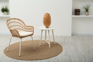 Stylish comfortable wicker armchair near table with lamp in room. Space for text