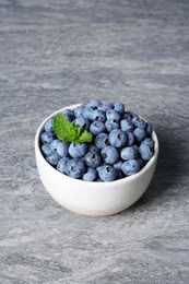 Photo of Bowl with juicy blueberries and green leaves on table