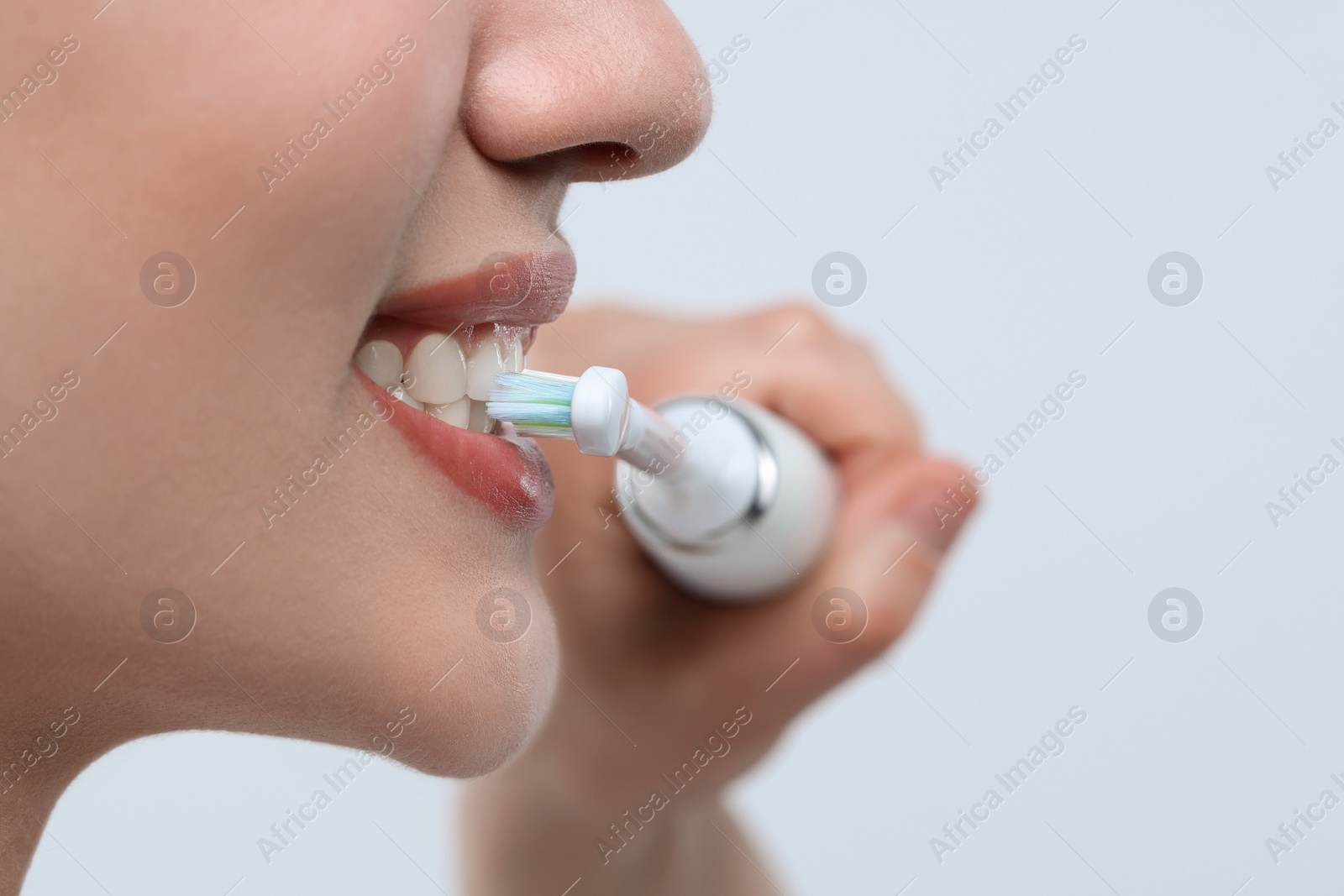 Photo of Woman brushing her teeth with electric toothbrush on white background, closeup. Space for text