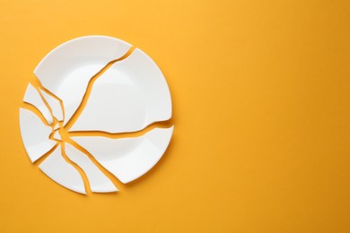 Photo of Pieces of broken ceramic plate on orange background, flat lay. Space for text