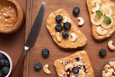 Photo of Toasts with tasty nut butter, blueberries, banana slices and cashews on brown table, flat lay