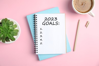 Image of Notebook with inscription 2023 Goals, cup of coffee, plant and pen on pink background, flat lay. New Year aims 