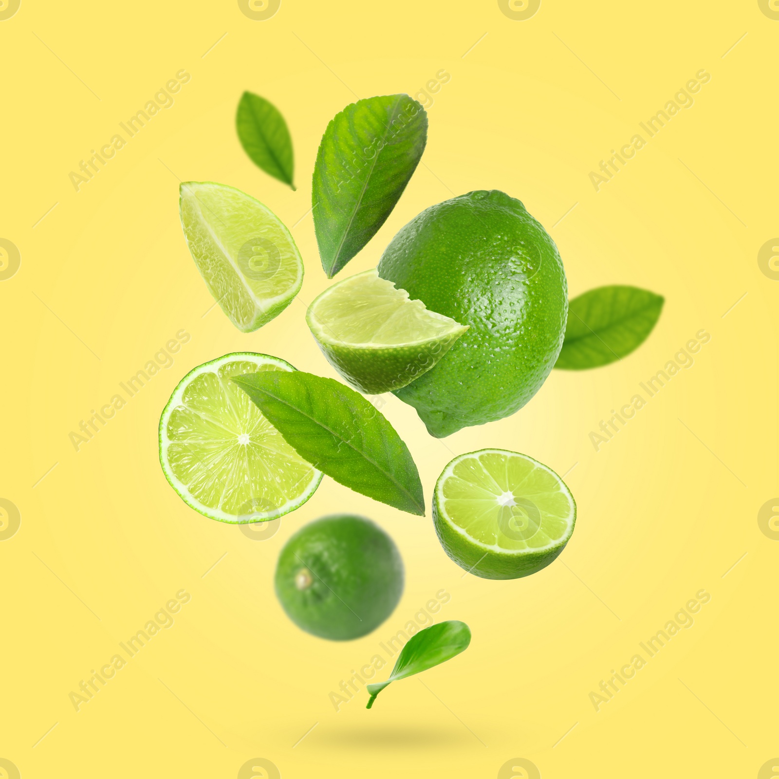 Image of Fresh lime fruits and green leaves falling on yellow background