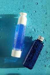 Bottles of cosmetic products on wet turquoise background, top view