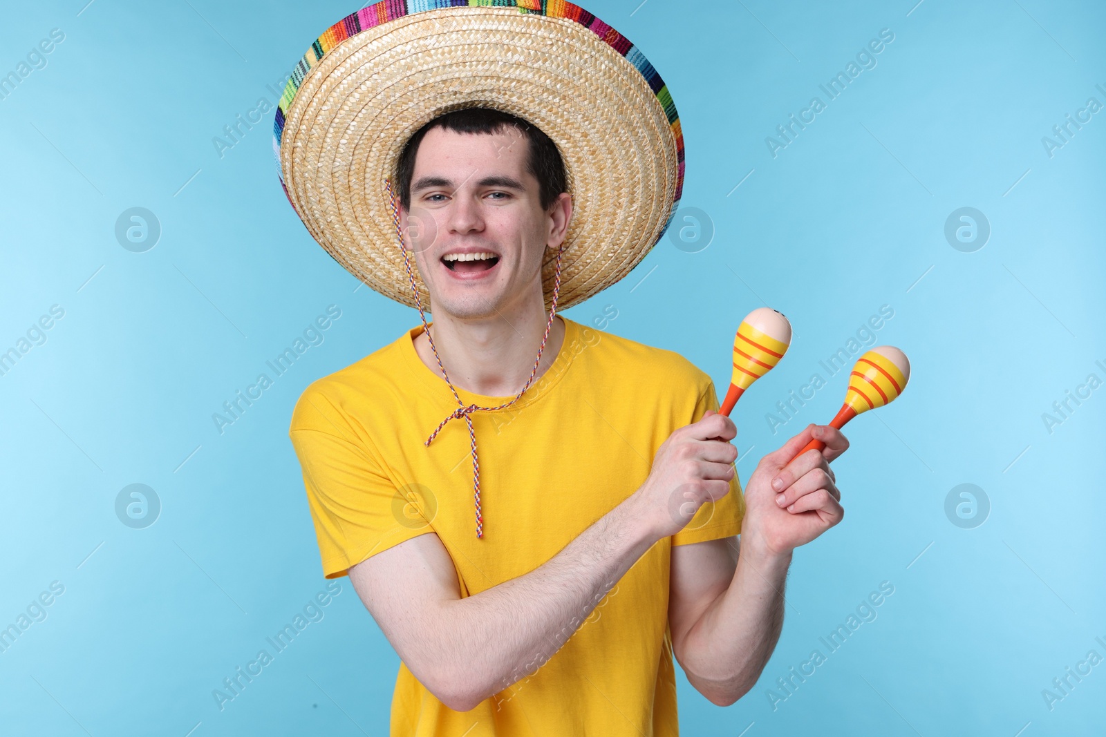 Photo of Young man in Mexican sombrero hat with maracas on light blue background