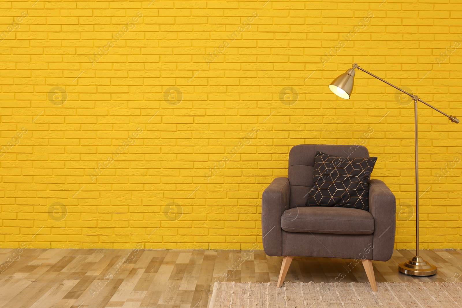 Photo of Stylish armchair and lamp near yellow brick wall in room, space for text. Interior design