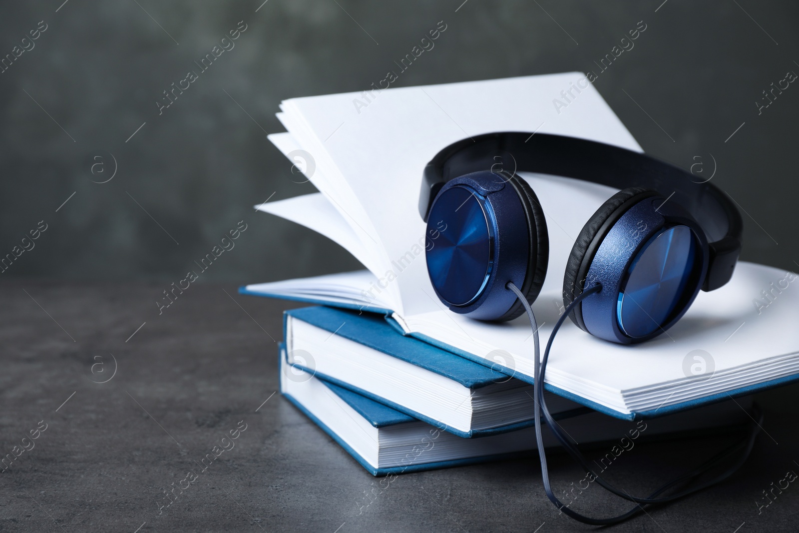 Photo of Modern headphones with hardcover books on grey table. Space for text