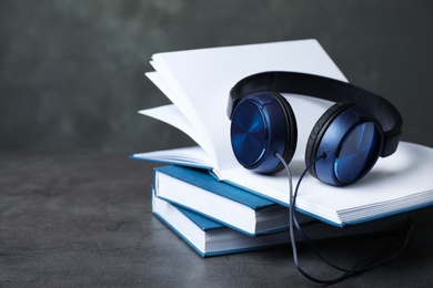 Photo of Modern headphones with hardcover books on grey table. Space for text