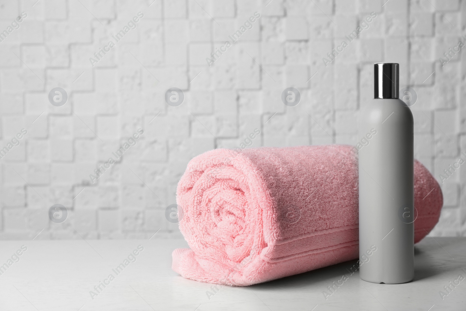 Photo of Bottle with shampoo and rolled bath towel on table, space for text