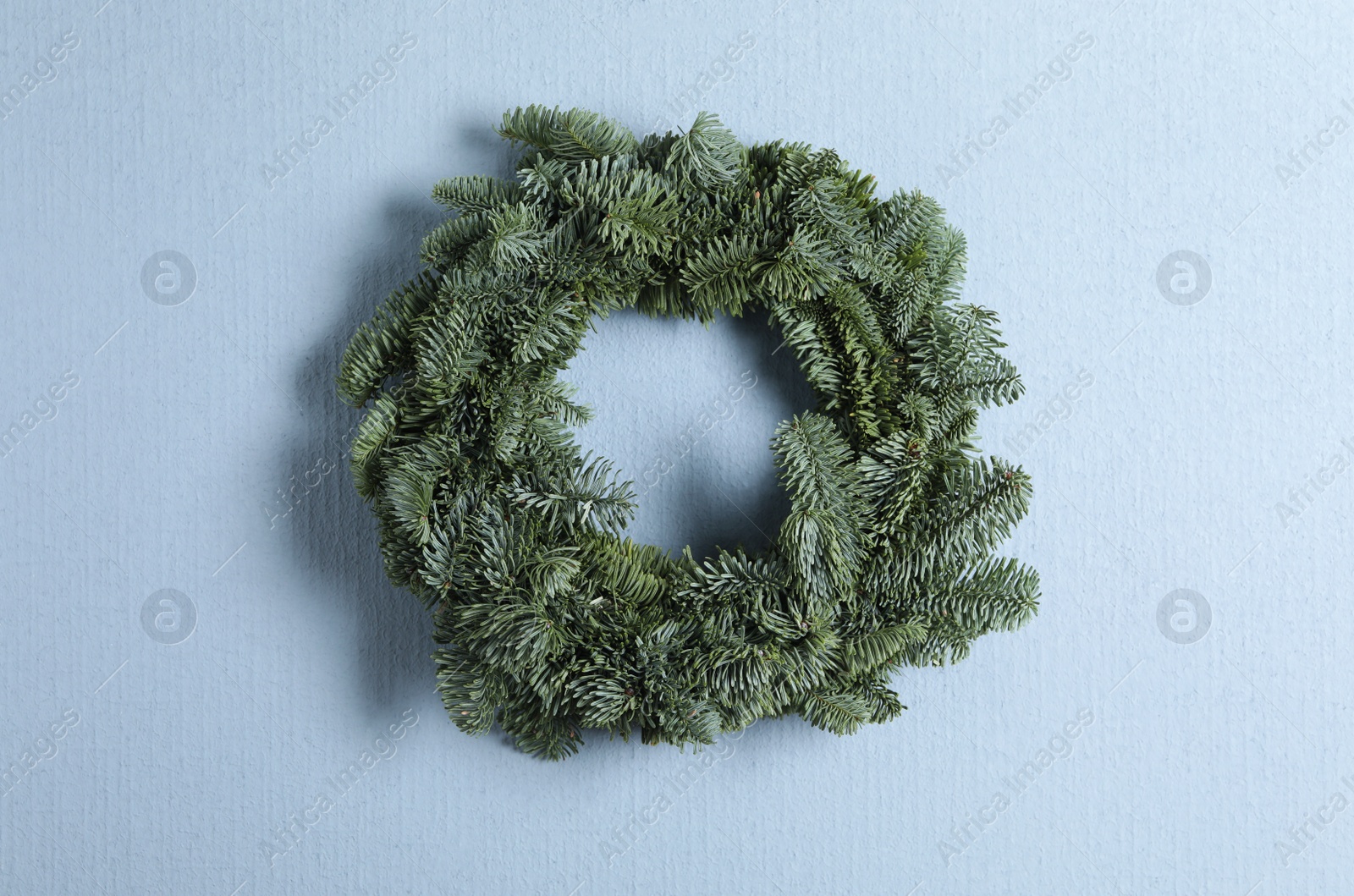 Photo of Christmas wreath made of fir tree branches on light blue background