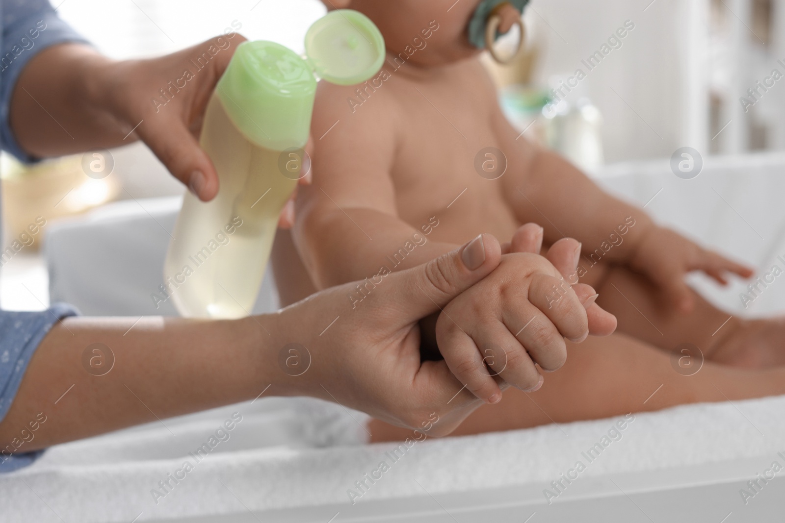 Photo of Mother massaging her baby with oil on changing table at home, closeup