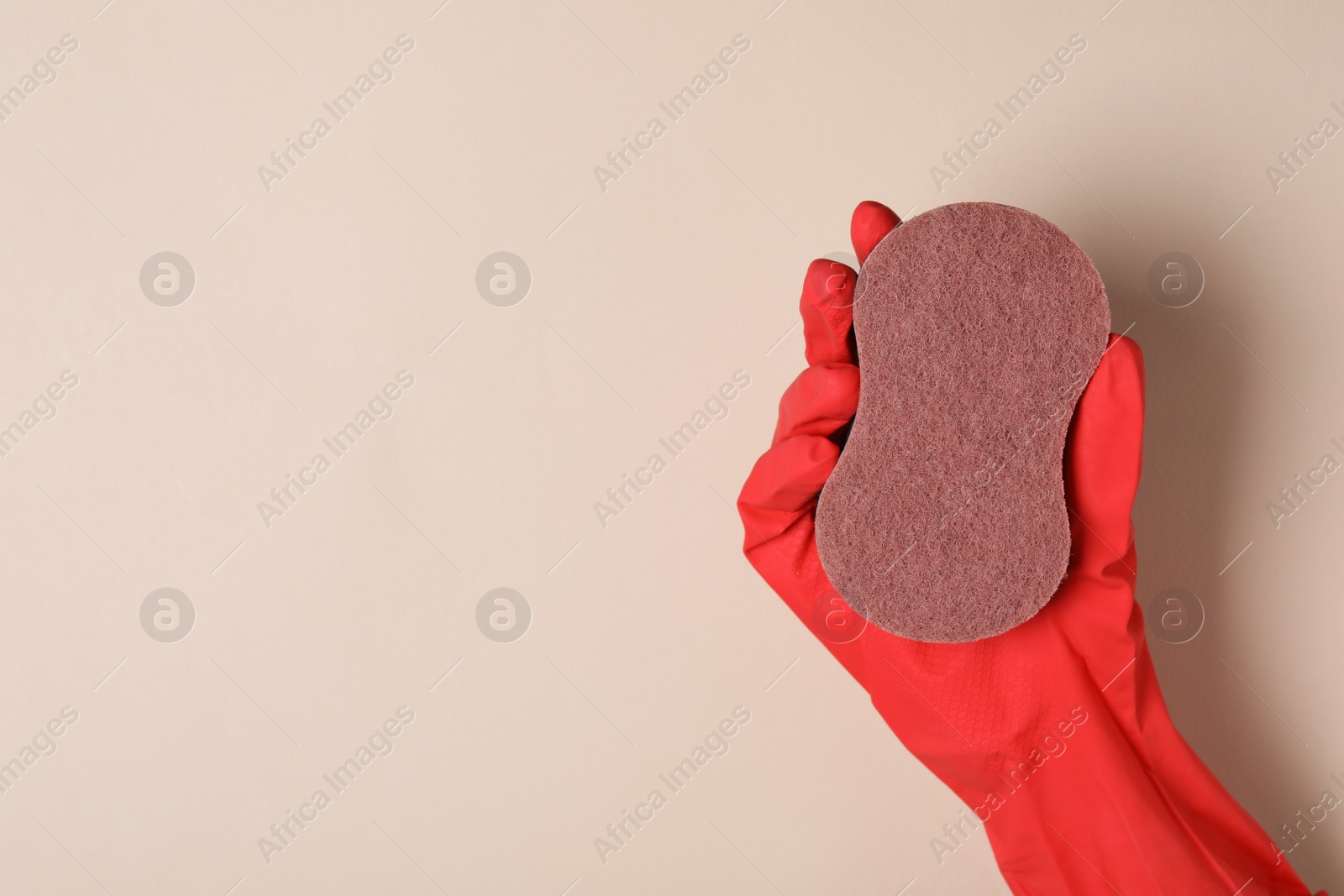 Photo of Woman in rubber glove holding sponge on beige background, top view. Space for text