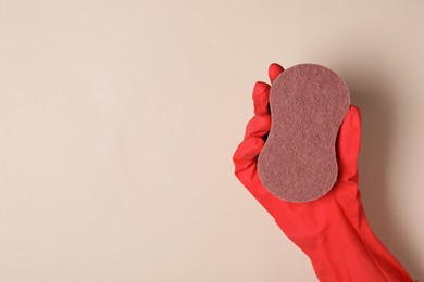 Woman in rubber glove holding sponge on beige background, top view. Space for text