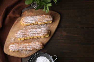 Photo of Delicious eclairs filled with cream, mint and powdered sugar on wooden table, top view. Space for text