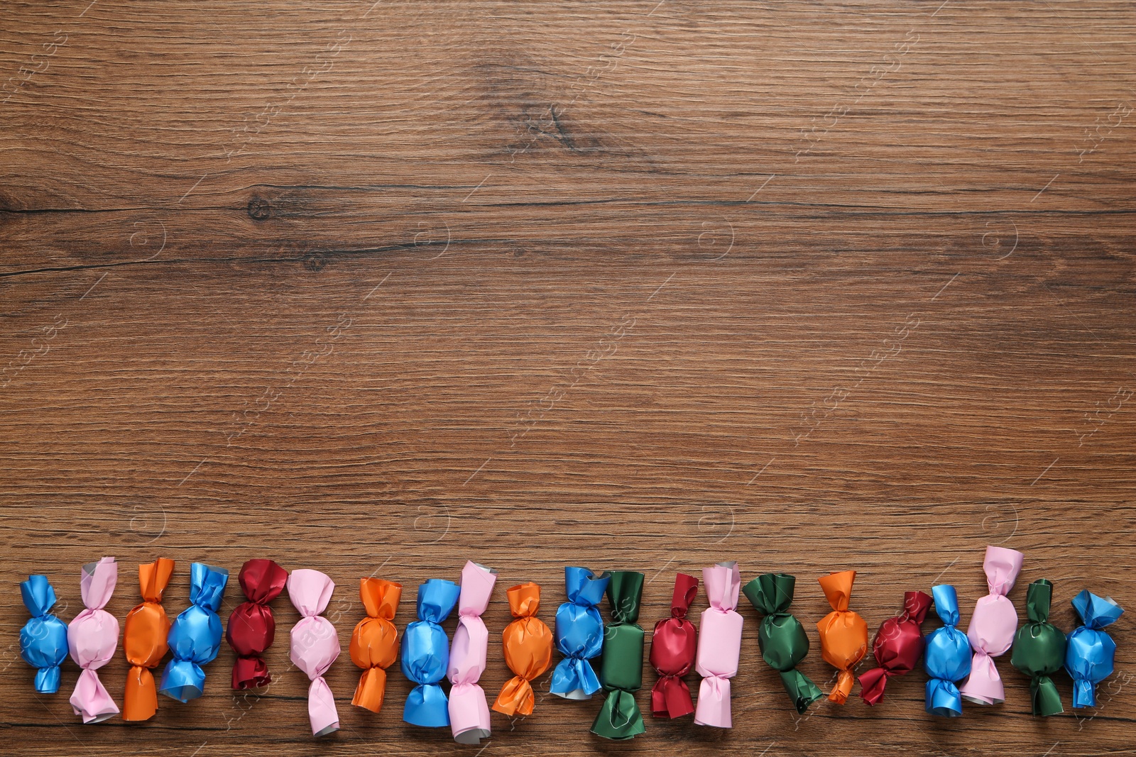 Photo of Many candies in colorful wrappers on wooden table, flat lay. Space for text