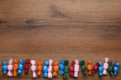 Many candies in colorful wrappers on wooden table, flat lay. Space for text