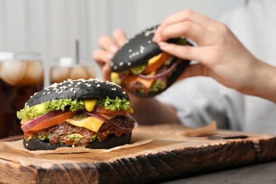 Photo of Tasty burger with black buns and woman eating on background