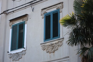 Photo of Old residential building with wooden shutters on windows and green tree