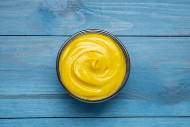 Photo of Sauce bowl with delicious mustard on light blue wooden table, top view