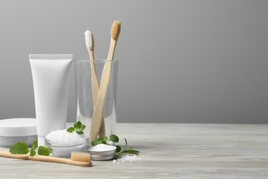 Toothbrushes, paste, green herbs and other teeth care products on wooden table, space for text