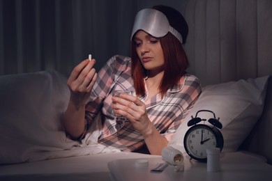 Woman suffering from insomnia taking pill in bed at night