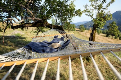 Comfortable net hammock with hat, book and blanket in mountains on sunny day
