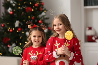Cute little girls with lollipops near Christmas tree at home