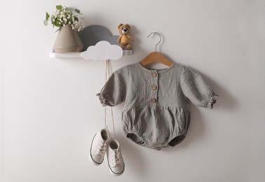 Photo of Cute children's baby onesie and shoes hanging on white wall