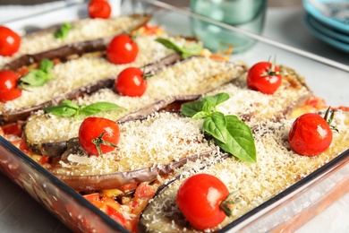 Baked eggplant with tomatoes, cheese and basil in dishware on table, closeup