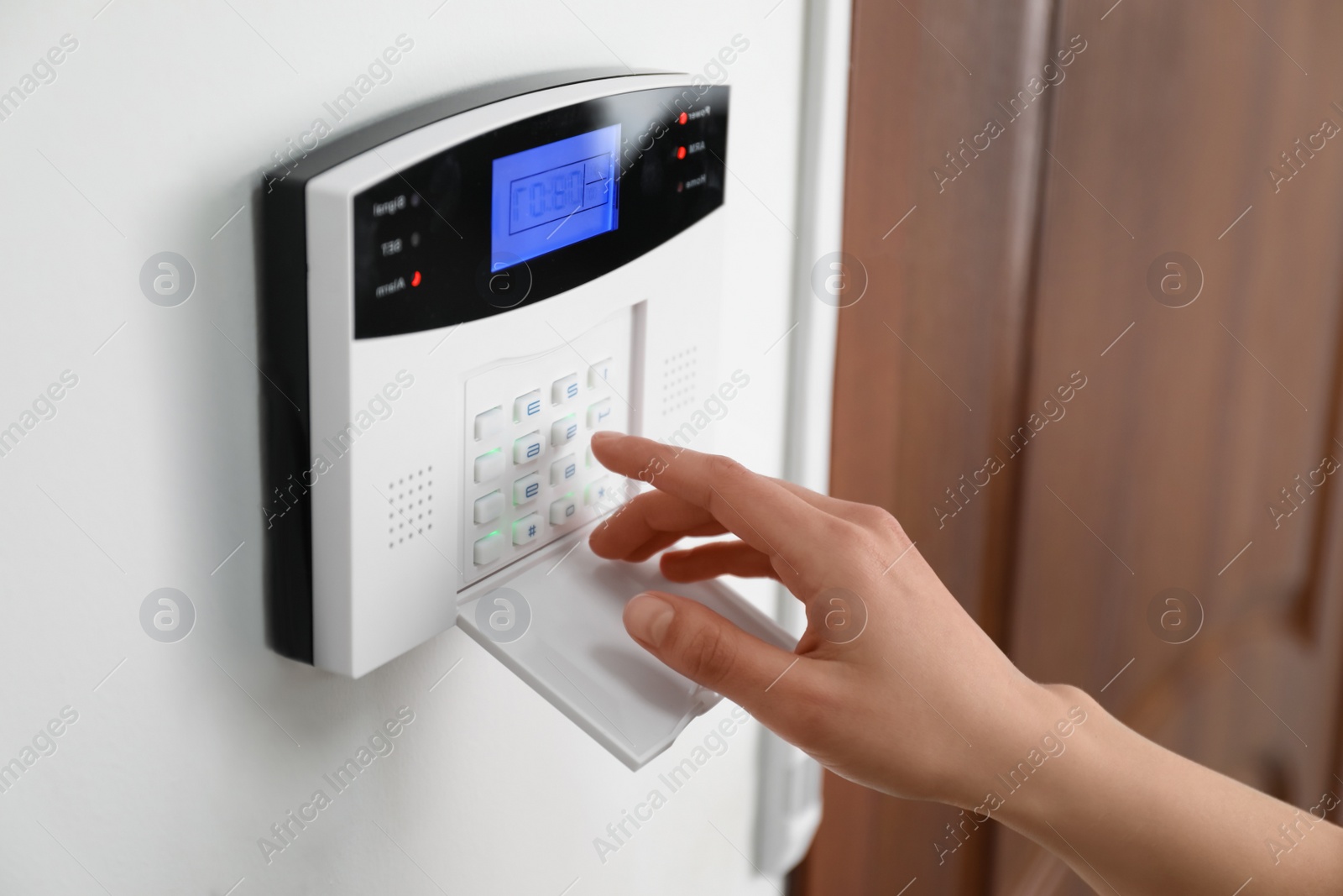 Photo of Woman entering code on home security system near door, closeup