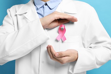 Photo of Mammologist with pink ribbon on light blue background, closeup. Breast cancer awareness