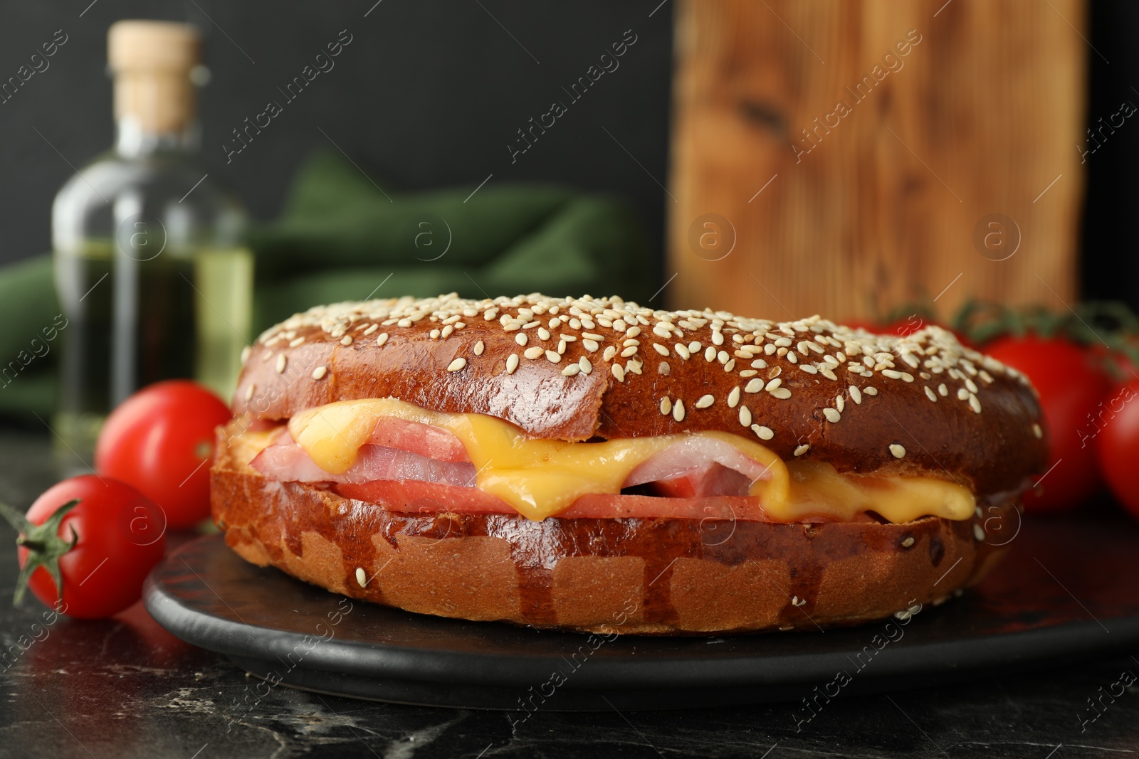 Photo of Delicious bagel with ham and cheese on dark marble table, closeup