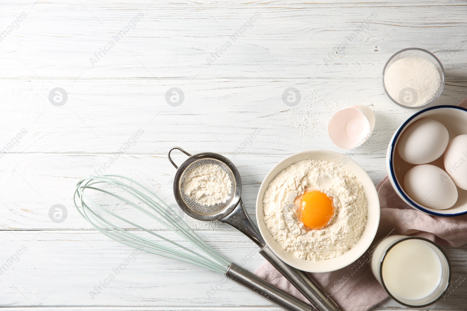 Photo of Flour with yolk in bowl and other ingredients for dough on white wooden table, flat lay. Space for text