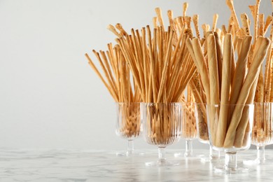 Photo of Delicious grissini sticks served in glasses on white marble table. Space for text