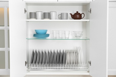 Open cabinet with different clean dishware in kitchen