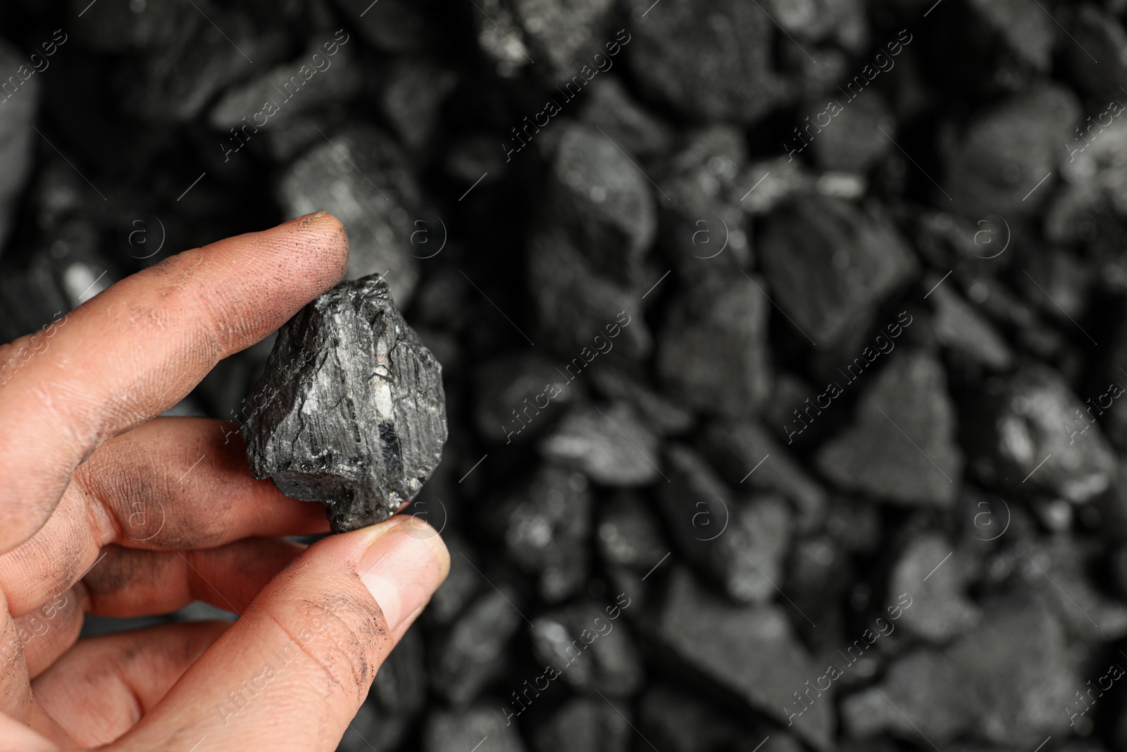 Photo of Man holding piece of coal over pile, closeup. Space for text