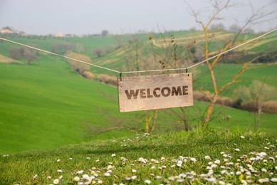 Welcome card. Wooden board with word hanging on rope in countryside