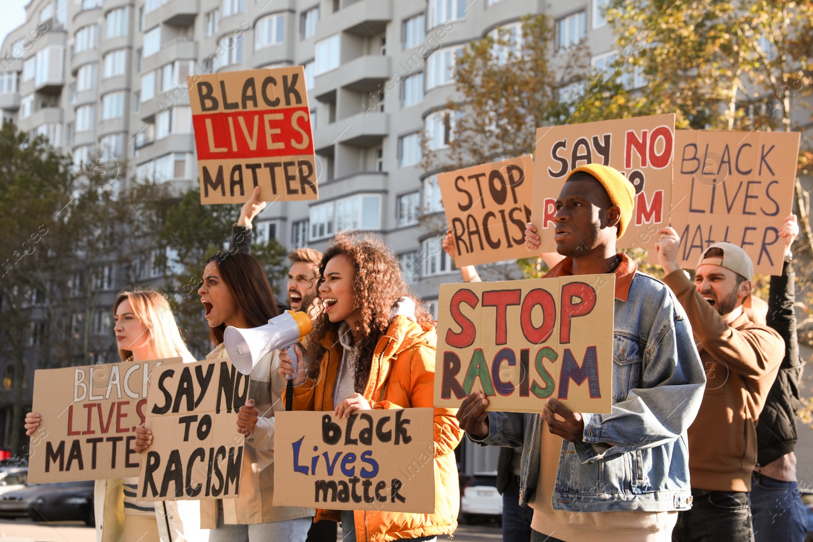 Photo of Protesters demonstrating different anti racism slogans outdoors. People holding signs with phrases