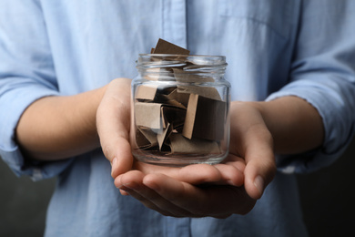 Woman holding glass jar with paper pieces, closeup on hands
