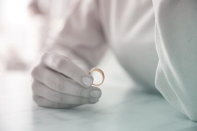 Image of Woman holding wedding ring at table indoors, closeup. Cheating and breakup