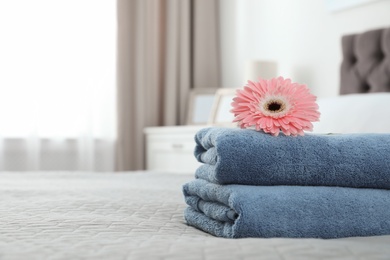 Stack of clean towels with flower on bed indoors. Space for text