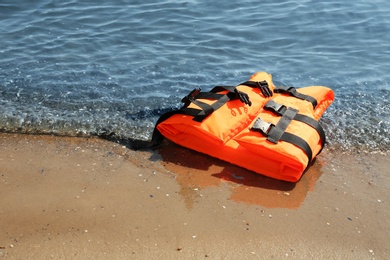 Photo of Orange life jacket on sand near sea. Emergency rescue equipment