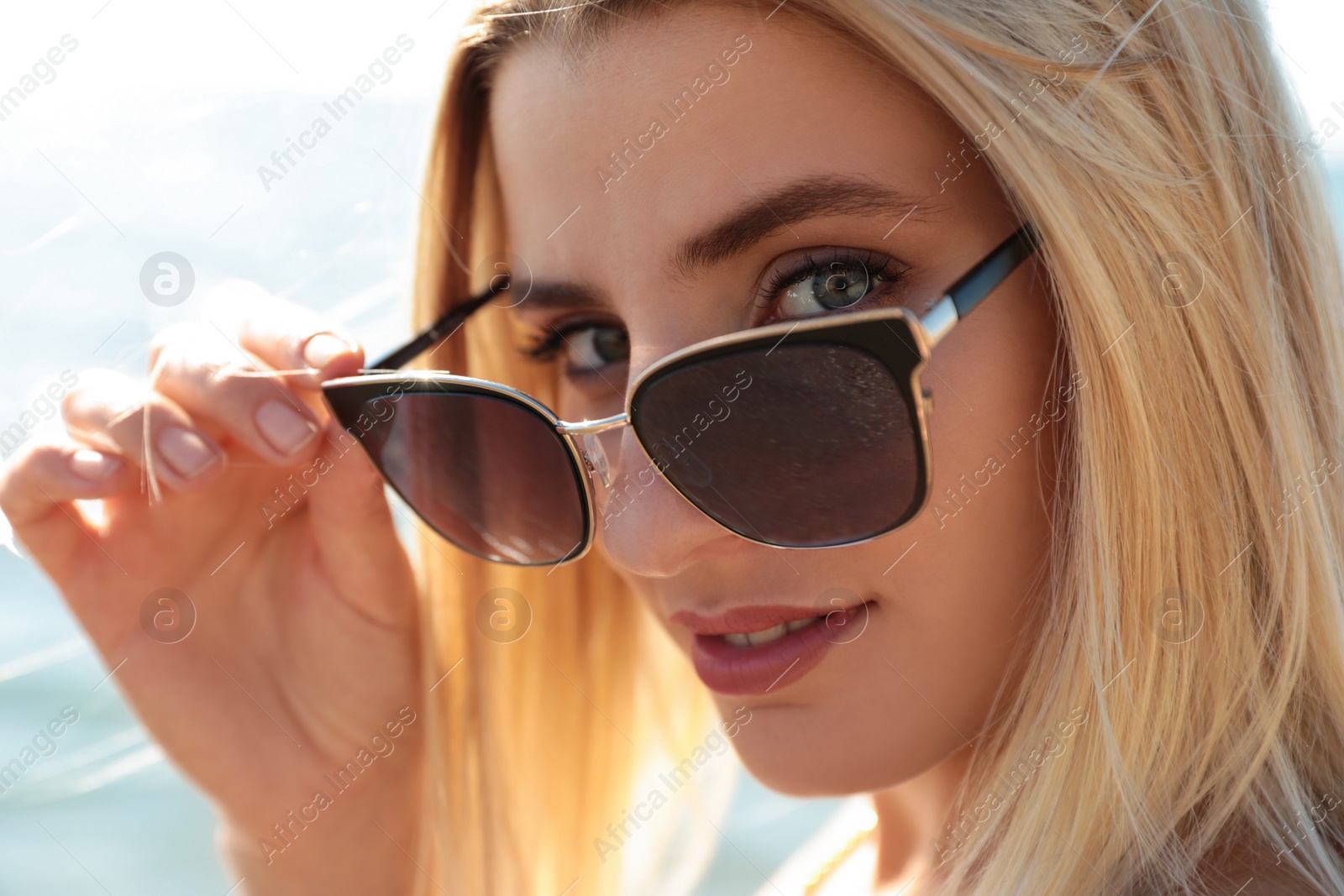 Photo of Beautiful woman wearing sunglasses near sea on sunny day, closeup
